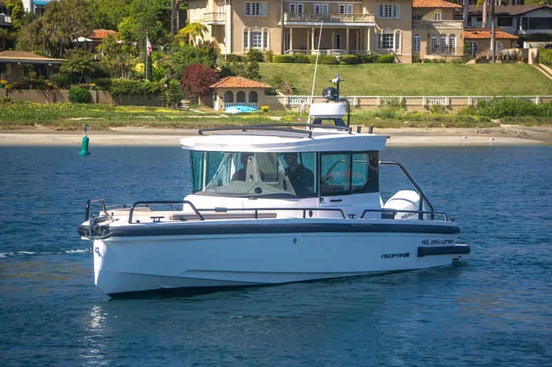  Yacht Photos Pics 2022 Axopar 28 Cabin boat cruising near a scenic shoreline with luxury homes.