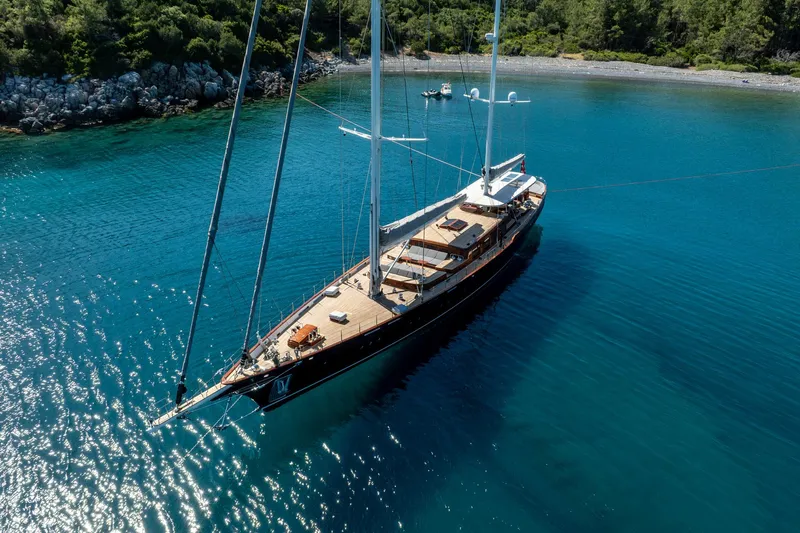 Sallyna Yacht Photos Pics Luxurious 2023 Su Marine sailing yacht anchored in clear turquoise waters near a rocky shoreline.