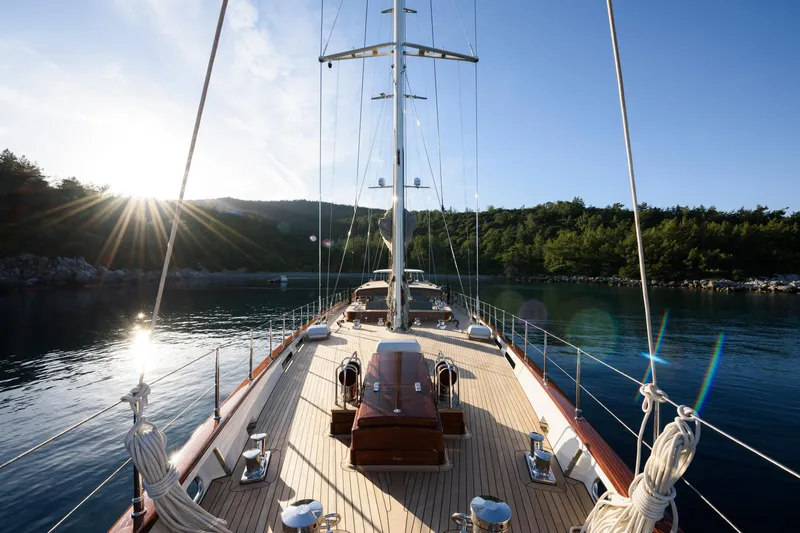 Sallyna Yacht Photos Pics Luxurious 2023 Su Marine sailing yacht on serene water with sunlit deck and lush shoreline.
