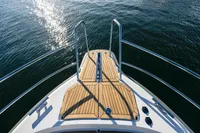 Bow of 2024 Nimbus 365 Coupe yacht with wooden deck and railing on water.