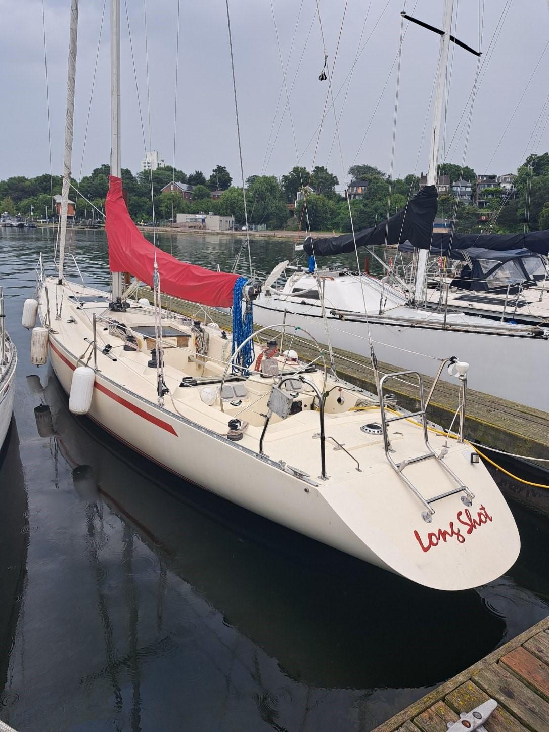 1986 Reliance 12m sailboat docked with red sail cover, calm water background.