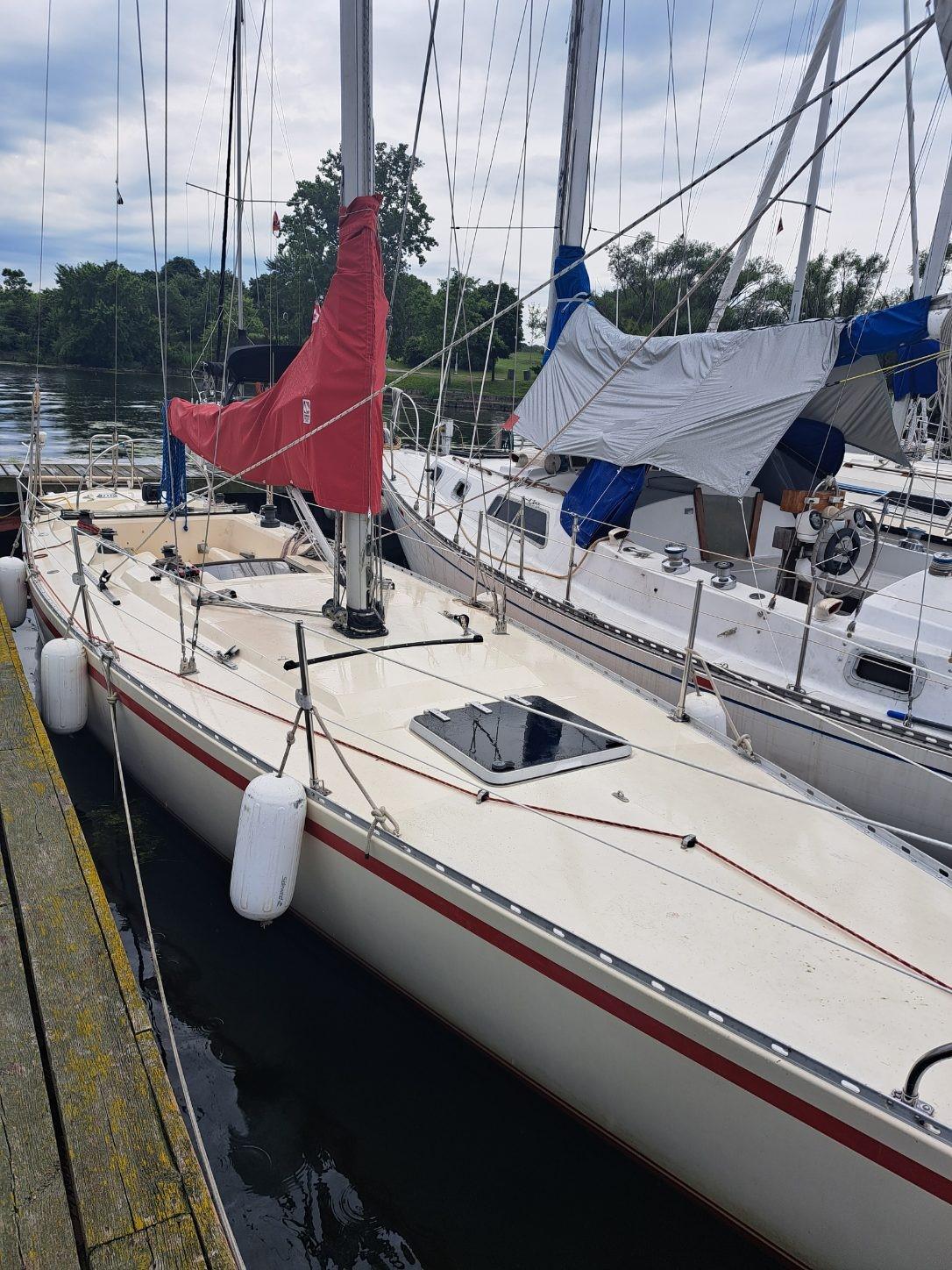 1986 Reliance 12m sailboat docked, featuring a red sail and white hull.