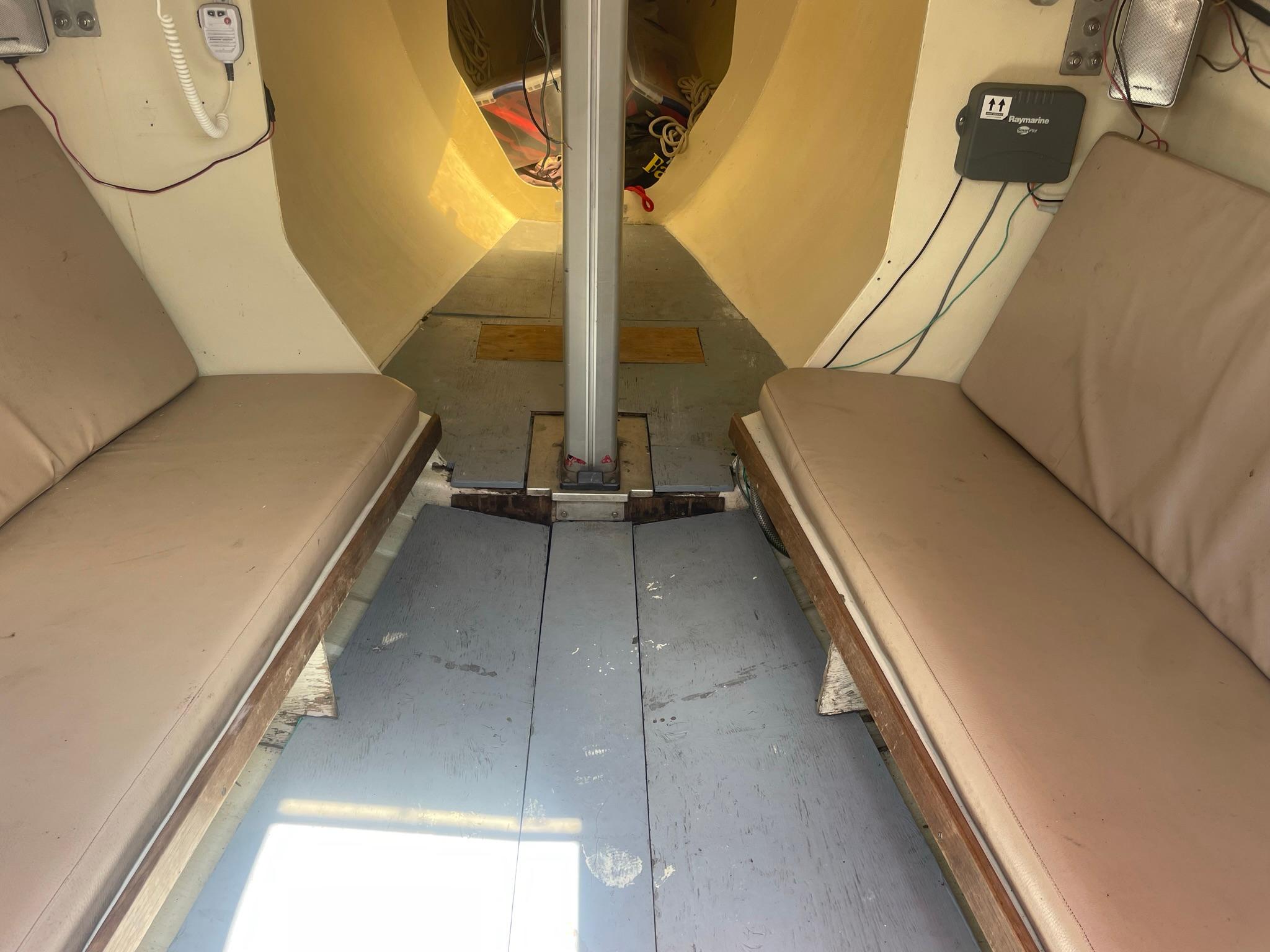 Interior of a 1986 Reliance 12m boat, featuring beige seating and a central mast.