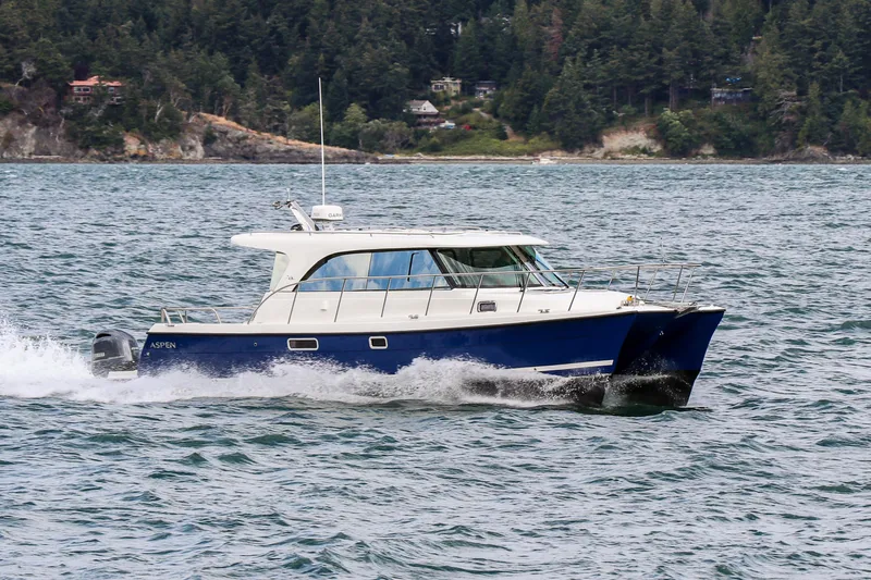  Yacht Photos Pics 2026 Aspen C108 boat cruising on a scenic lake with forested shoreline.
