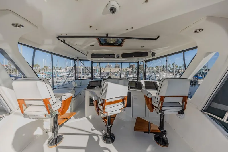 Kolohe Yacht Photos Pics Interior view of 1993 Ocean 65 Custom yacht helm with three chairs and marina backdrop.