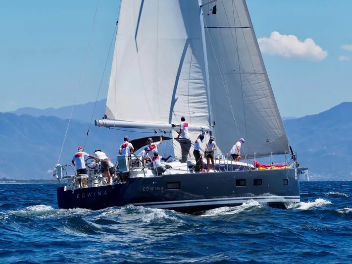 Edwina Yacht Photos Pics 2018 Jeanneau 54 sailboat navigating ocean waters with crew, mountains in background.
