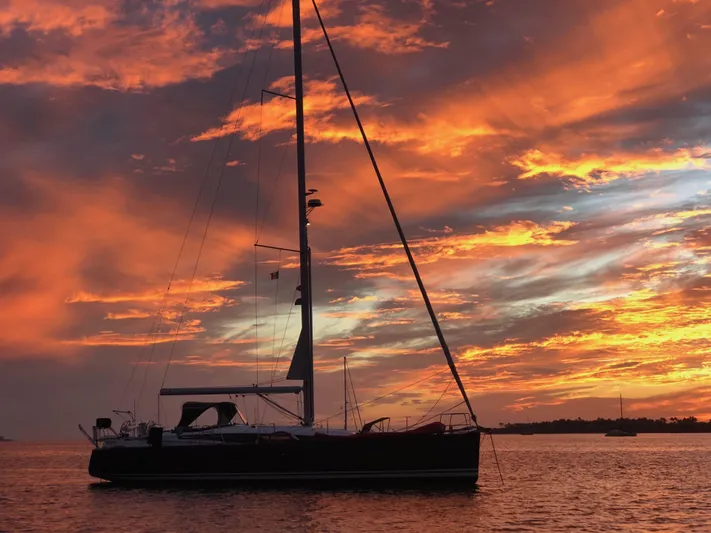 Edwina Yacht Photos Pics Sailing yacht Jeanneau 54 (2018) silhouetted against a vibrant sunset sky.