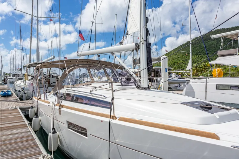 Off The Clock Yacht Photos Pics 2020 Jeanneau Sun Odyssey 349 sailboat docked at marina, clear sky, lush hillside background.