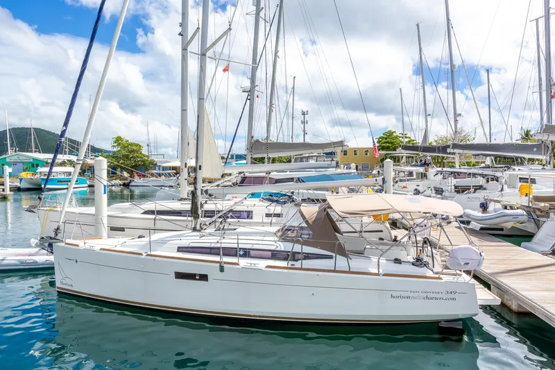 Off The Clock Yacht Photos Pics 2020 Jeanneau Sun Odyssey 349 sailboat docked in a marina under a cloudy sky.
