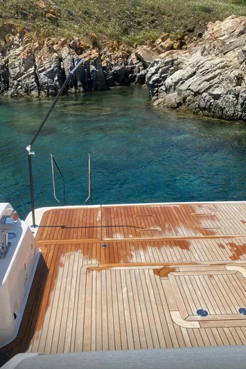  Yacht Photos Pics 2024 Bluegame BG54 yacht with wooden deck near rocky shoreline and clear blue water.