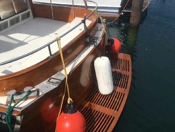 Blackjack Yacht Photos Pics 1984 Midnight Lace Rumrunner boat stern with fenders and wooden deck, docked in calm water.