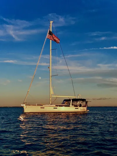 Lucky Yacht Photos Pics 2014 Beneteau Oceanis 45 sailboat on calm water at sunset with American flag.