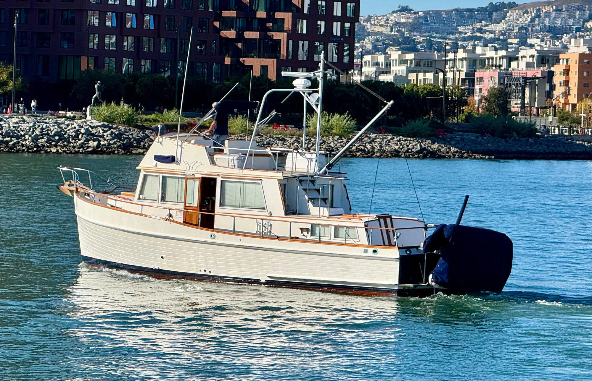 1979 Grand Banks Classic yacht cruising near urban waterfront.