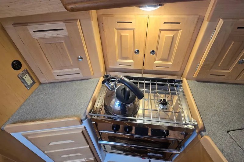Irie Yacht Photos Pics Compact kitchen in 2018 Tartan 345 yacht with stove, kettle, and wooden cabinets.