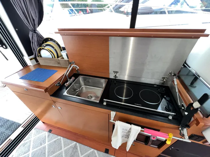  Yacht Photos Pics 2017 Jeanneau NC11 yacht kitchen with sink, stove, and wooden cabinetry.