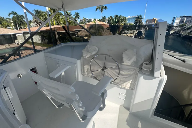 Music Yacht Photos Pics 1989 Hatteras 65 Motor Yacht helm with steering wheel and chair, docked near palm trees.