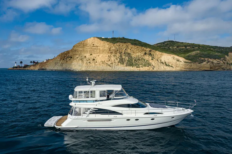 Desperado Yacht Photos Pics 2002 Fairline Squadron 58 yacht cruising near a rocky coastline under a blue sky.
