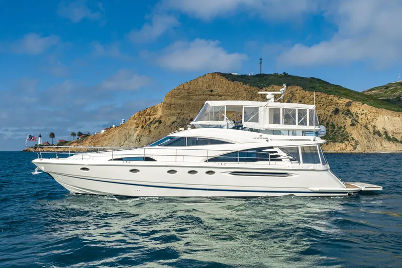 Desperado Yacht Photos Pics 2002 Fairline Squadron 58 yacht cruising near a rocky coastline under a clear blue sky.