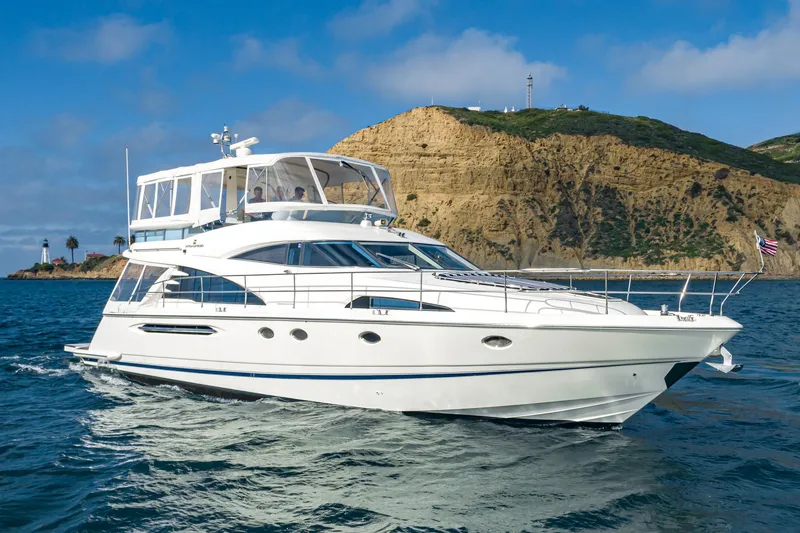 Desperado Yacht Photos Pics 2002 Fairline Squadron 58 yacht cruising near a rocky coastline under a clear blue sky.