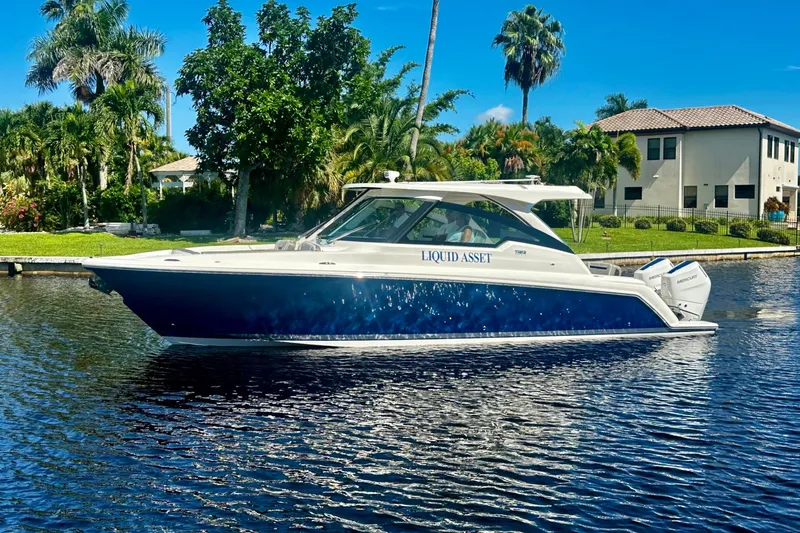 Liquid Asset Yacht Photos Pics 2024 Tiara Yachts 34 LX on water, surrounded by lush greenery and waterfront homes.