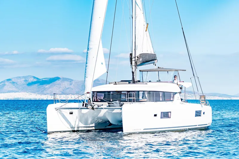  Yacht Photos Pics 2018 Lagoon 42 catamaran sailing on clear blue waters with mountainous backdrop.