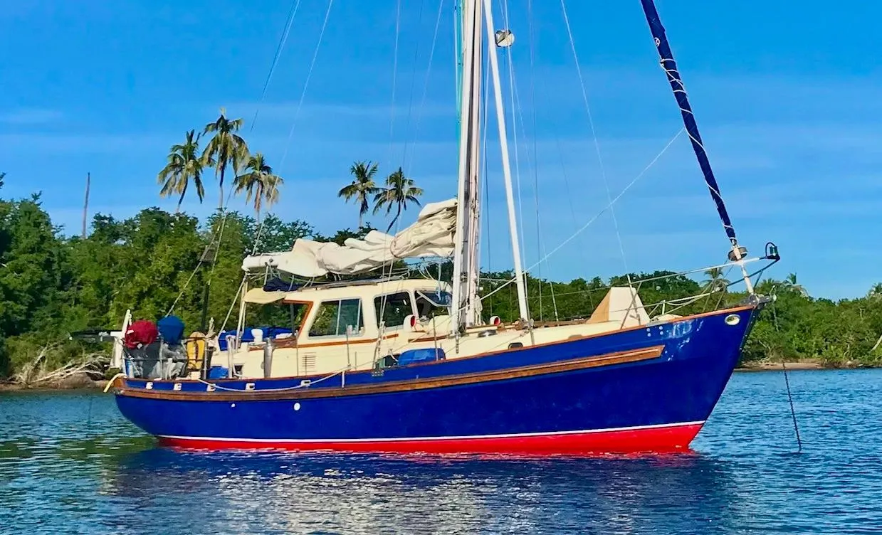 1975 Salar 40 sailboat with blue hull anchored near tropical shoreline.
