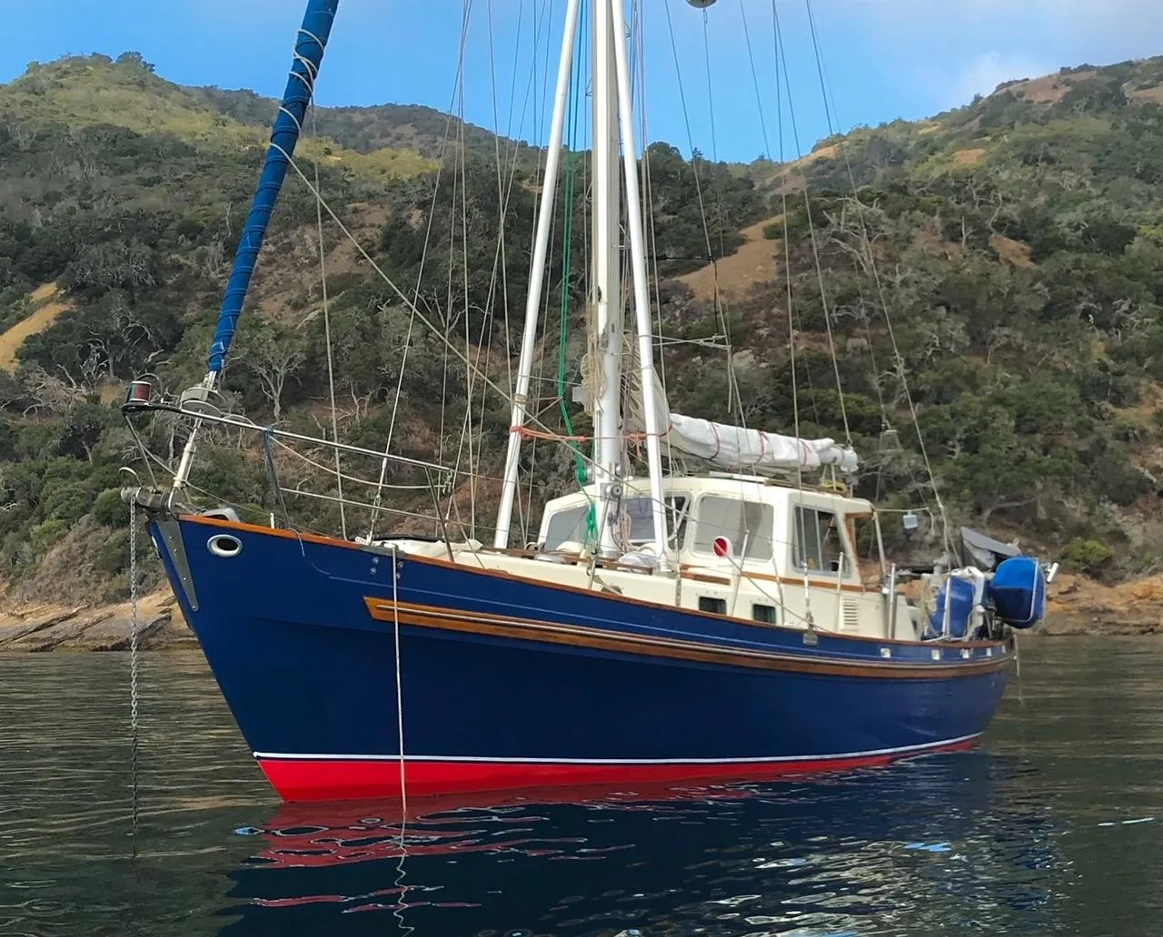 1975 Salar 40 sailboat with blue hull, anchored near a scenic coastline.
