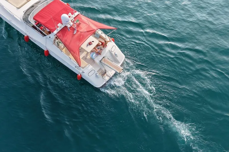 Yacht Photos Pics Aerial view of 1989 Riva 51 Turborosso yacht with red canopy cruising on blue water.