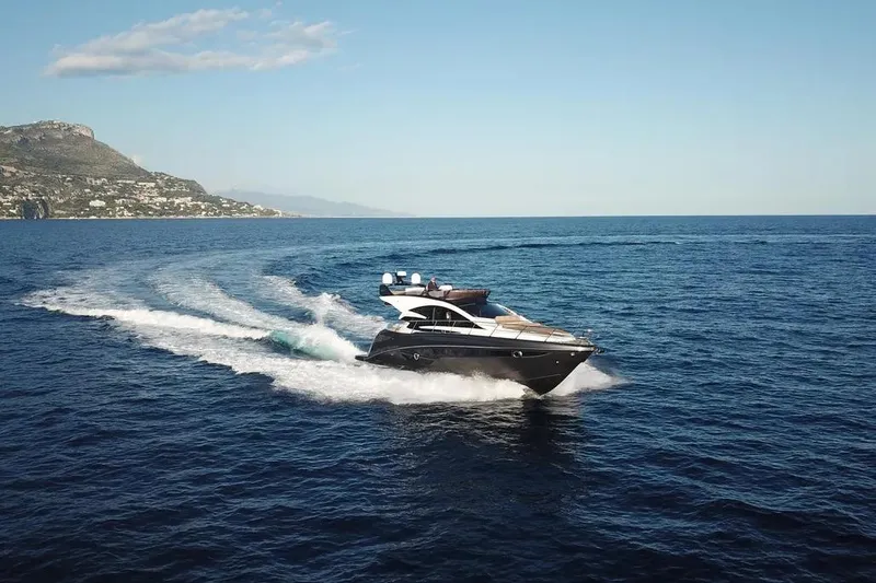  Yacht Photos Pics 2025 Cobrey 52 FLY yacht cruising on open sea with scenic coastal backdrop.