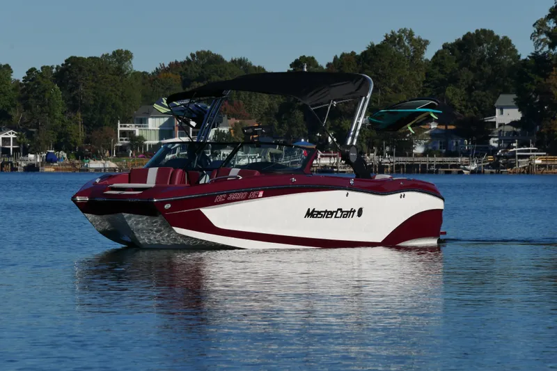  Yacht Photos Pics 2022 MasterCraft X22 boat on a lake, surrounded by trees and houses.