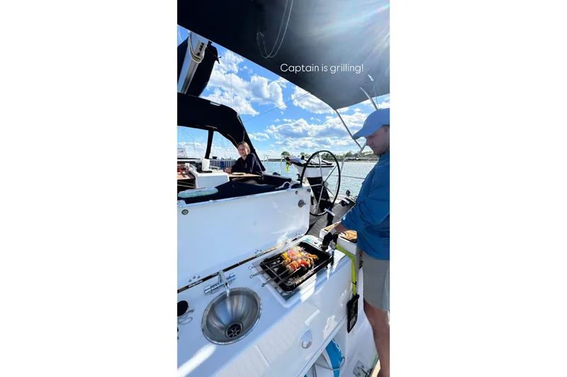 Squeeze De Citron Yacht Photos Pics Man grilling on a 2023 Dufour 37 sailboat under sunny skies.