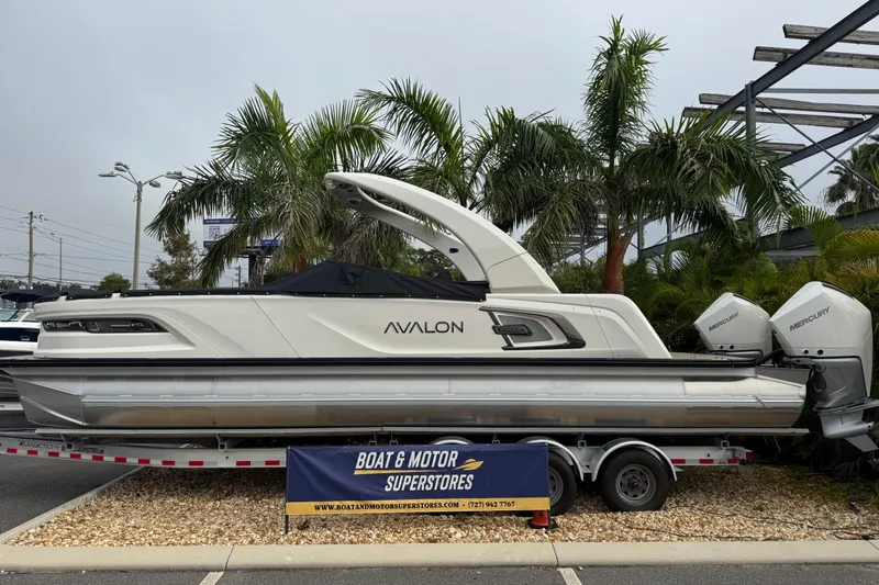  Yacht Photos Pics 2026 Avalon Excalibur 27' boat on trailer at dealership, surrounded by palm trees.