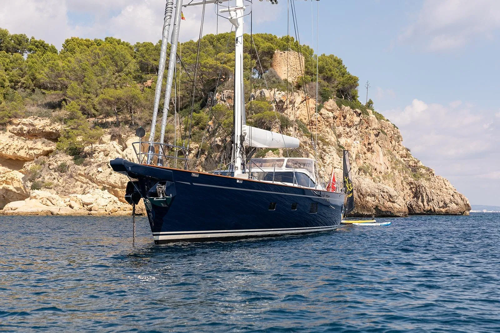 Sailing yacht by Steve Ward & Co, 2009, anchored near rocky coastline with lush greenery.