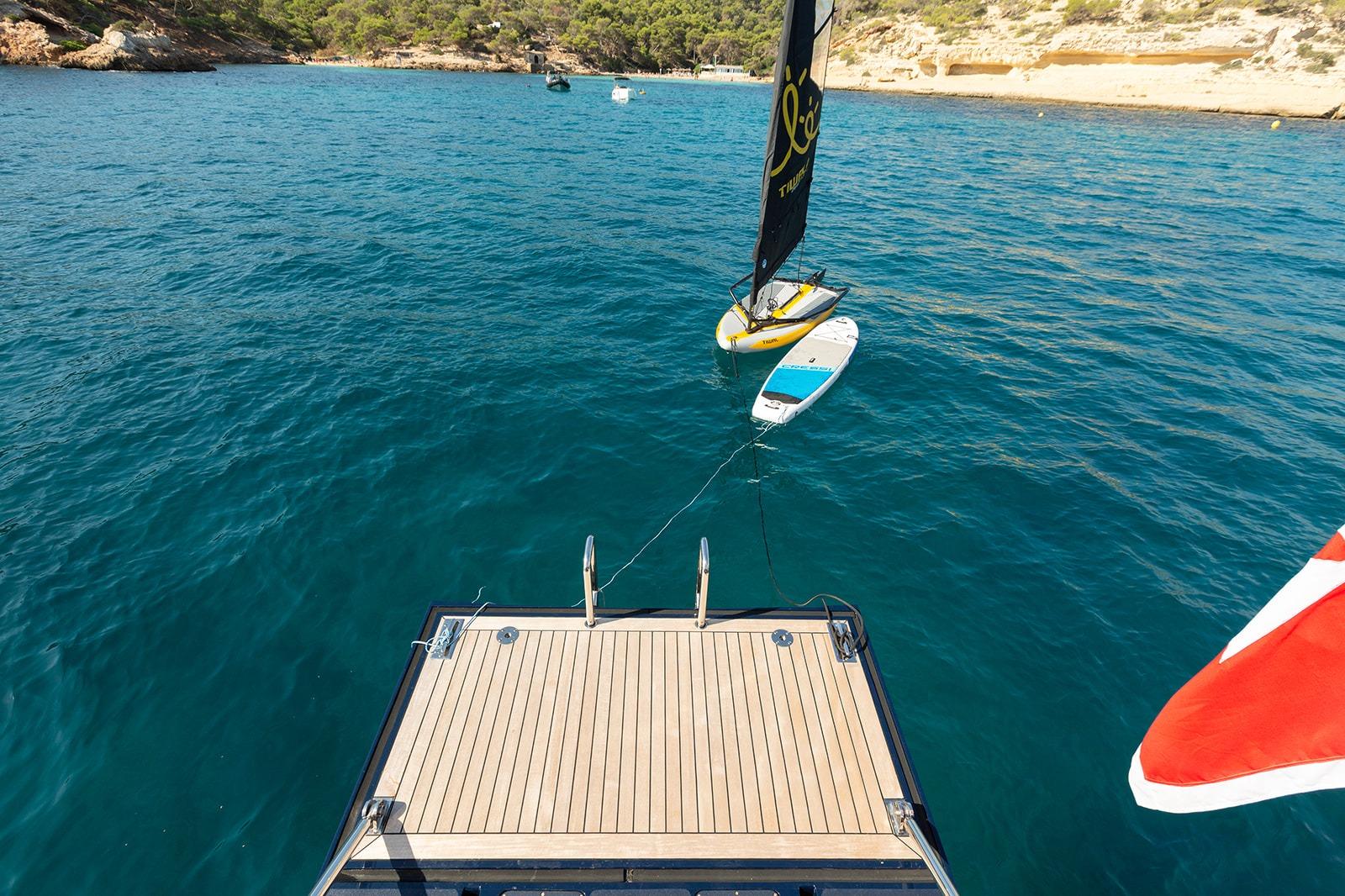 Luxury yacht deck with paddleboard and sailboat on clear blue water, Steve Ward & Co Custom 2009.