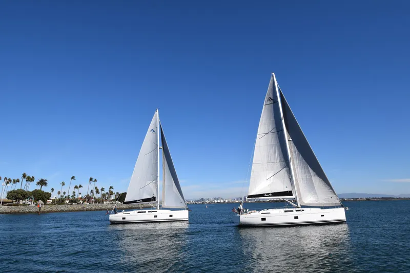 Hanse 418 #303 San Yacht Photos Pics Two 2023 Hanse 418 sailboats on a sunny day, sailing near a palm-lined shore.