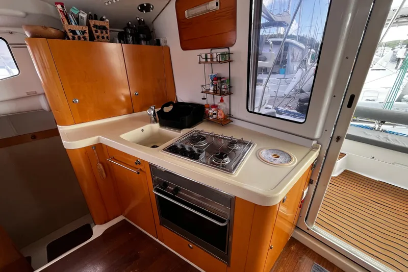  Yacht Photos Pics 2007 Fountaine Pajot Mahe 36 yacht kitchen with stove, sink, and wooden cabinetry.
