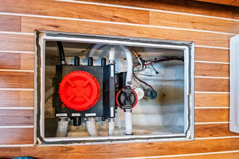 "double Down" Yacht Photos Pics Boat bilge compartment with plumbing and wiring, featuring a red valve, on wooden flooring.