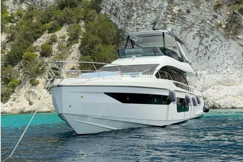  Yacht Photos Pics Luxury 2022 Azimut 68 yacht anchored near rocky coastline with clear blue water.