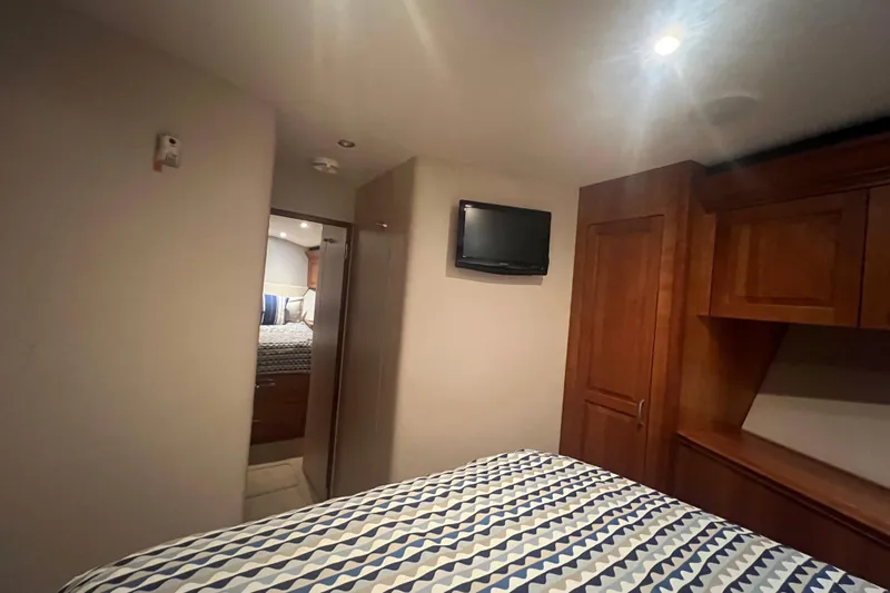 Sixpack Yacht Photos Pics 2013 Hatteras GT63 yacht bedroom with patterned bedding, wooden cabinets, and wall-mounted TV.