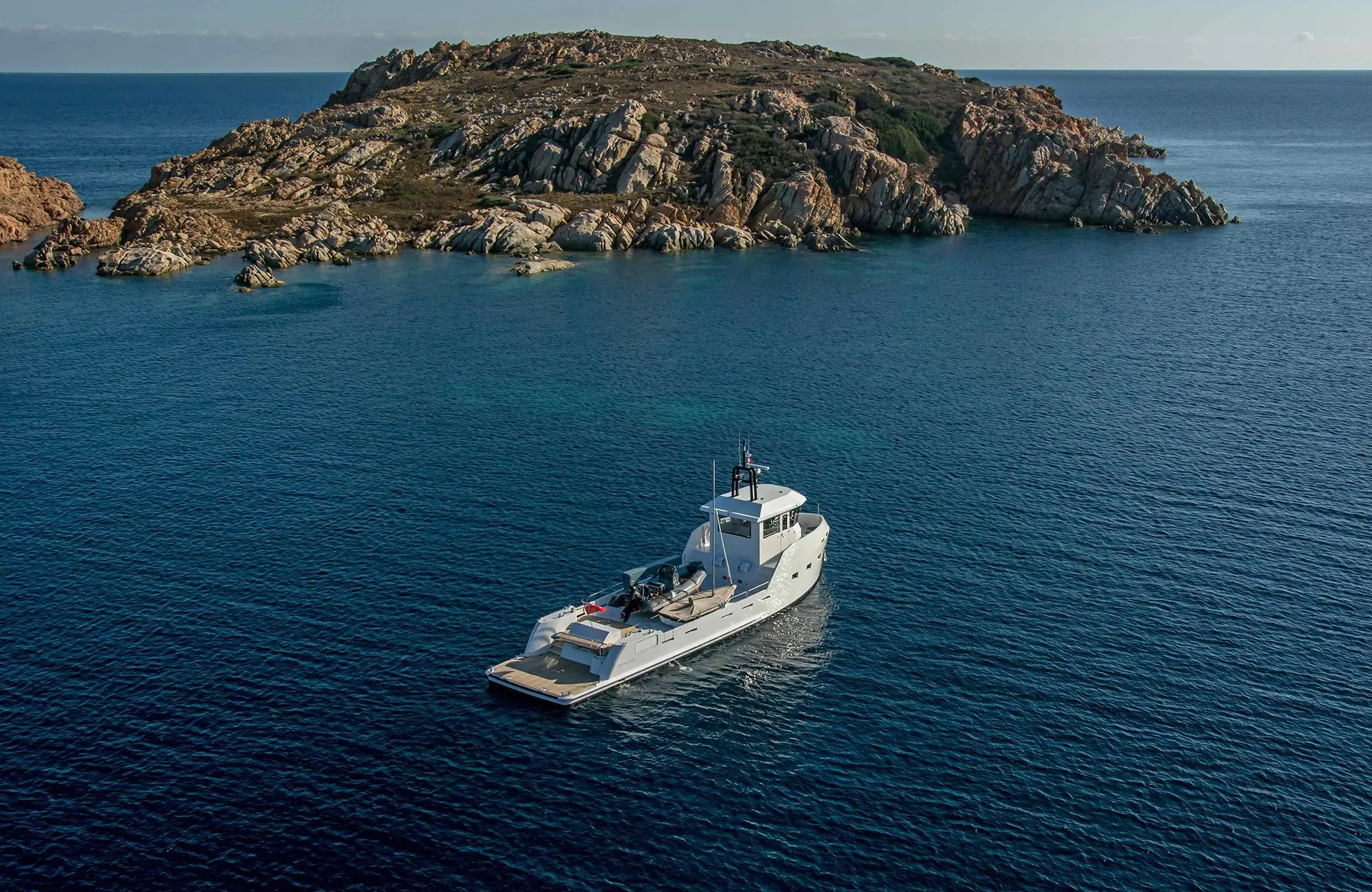 Outer Reef Yachts 20 YXT 2027 cruising near rocky island in serene blue waters.