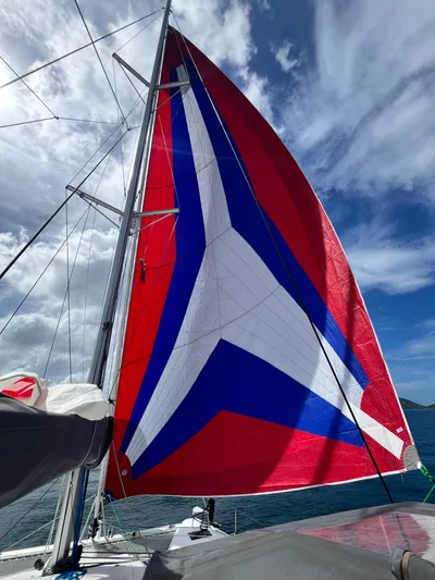 Family Therapy Yacht Photos Pics 2023 Fountaine Pajot Elba 45 sailboat with vibrant red, blue, and white sail against cloudy sky.