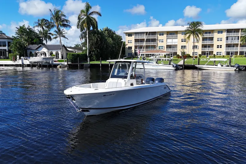  Yacht Photos Pics 2022 Pursuit S 288 Sport boat on calm water near waterfront buildings and palm trees.