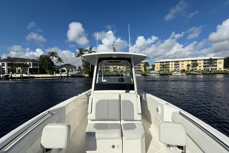  Yacht Photos Pics 2022 Pursuit S 288 Sport boat on calm water, with waterfront buildings in the background.