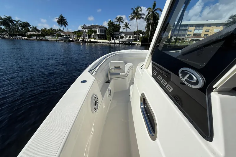  Yacht Photos Pics 2022 Pursuit S 288 Sport boat on calm water, with palm trees and buildings in the background.