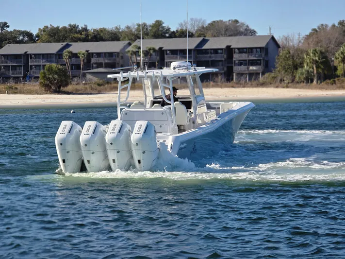  Yacht Photos Pics 2024 Invincible 43 Open Fisherman boat with four engines cruising near a sandy shoreline.