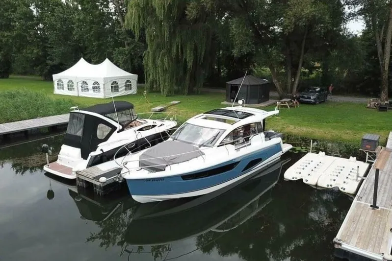  Yacht Photos Pics 2023 Sealine C335V yacht docked beside another boat, surrounded by lush greenery.