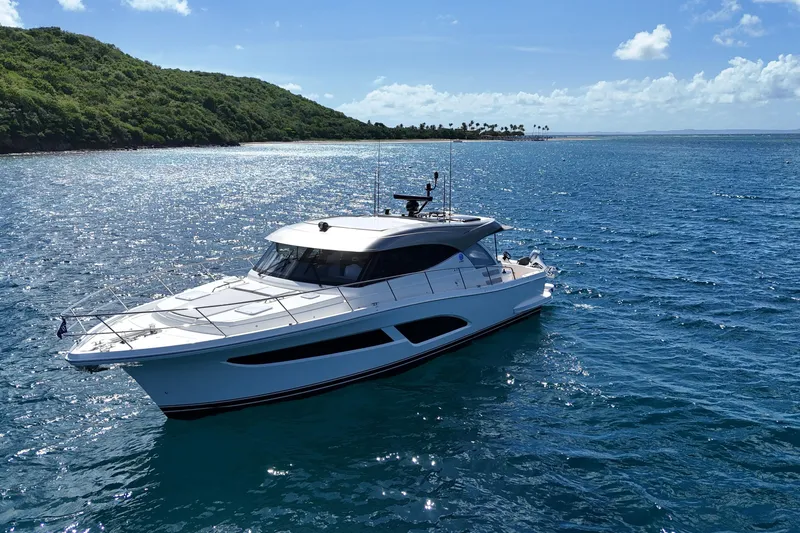  Yacht Photos Pics 2023 Riviera 465 SUV yacht cruising on clear blue ocean near lush green island.
