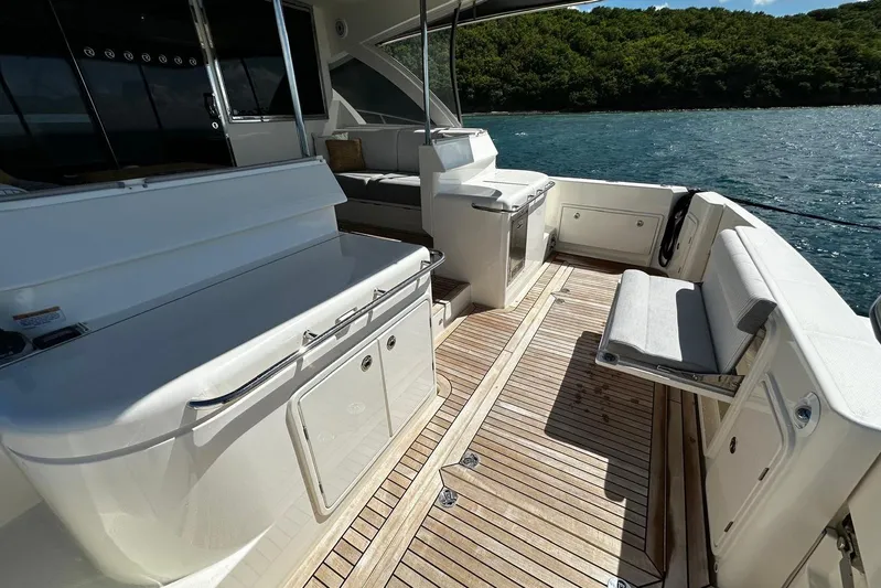  Yacht Photos Pics 2023 Riviera 465 SUV yacht deck with seating, overlooking serene water and lush greenery.