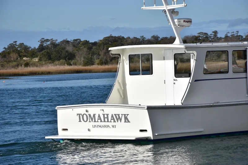 Tomahawk Yacht Photos Pics White boat named "Tomahawk" on water, near a wooded shoreline.