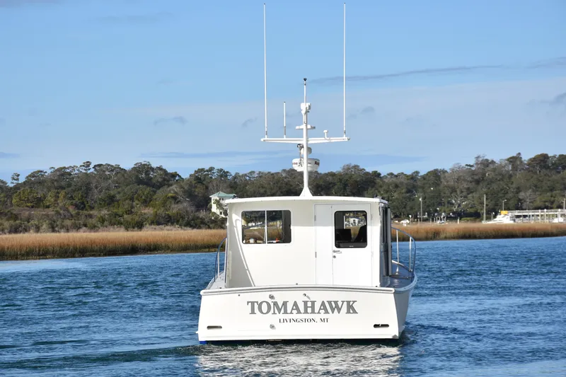 Tomahawk Yacht Photos Pics Boat named "Tomahawk" on water, surrounded by trees, clear sky.